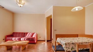 Ein Zimmer mit einem Holztisch, einem roten Sofa, einem hölzernen Bett mit einer blumigen Tischdecke und zwei Pendelleuchten.