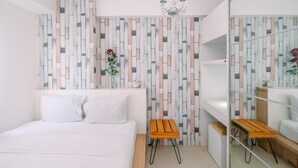 Une chambre à coucher moderne avec un lit, un tabouret en bois, un miroir et un mur orné d’un motif géométrique.