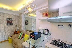A modern kitchen with a glass countertop, a gas stove, and a coffee maker. There is a sofa with cushions and a small table with a basket of bottled water.
