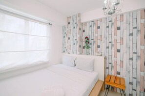 A bedroom with a bed, a bedside table, a window with curtains, and a wall with a decorative panel.