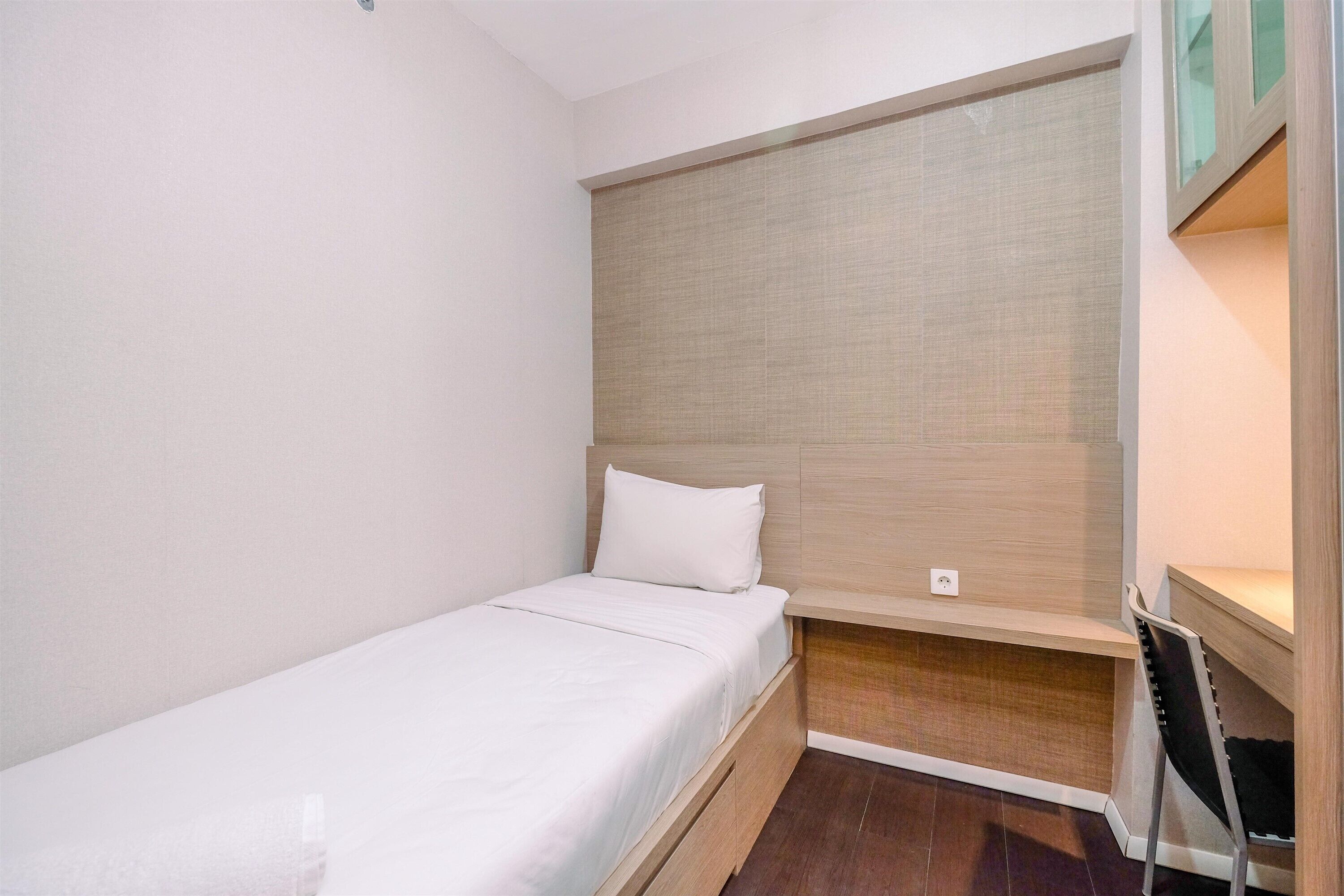 A small, single-bed room with a wooden headboard, a desk, and a chair.
