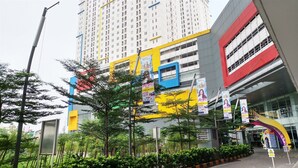 A modern building with a yellow and blue facade, surrounded by greenery and featuring multiple banners advertising events. - Nice And Fresh 2Br At Bassura City Apartment (Jakarta)
