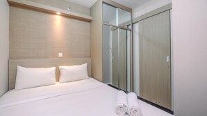 A hotel room with a bed, a wooden headboard, a glass door closet, and a wall-mounted light. - Nice And Fresh 2Br At Bassura City Apartment (Jakarta)