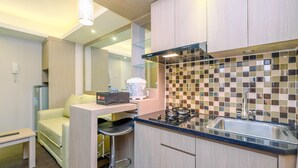 A compact kitchen with a gas stove, a sink, and a microwave. There is a small seating area with a sofa and a table. - Nice And Fresh 2Br At Bassura City Apartment (Jakarta)
