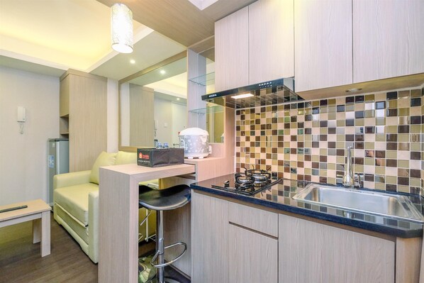 A compact kitchen with a gas stove, a sink, and a microwave. There is a small seating area with a sofa and a table.