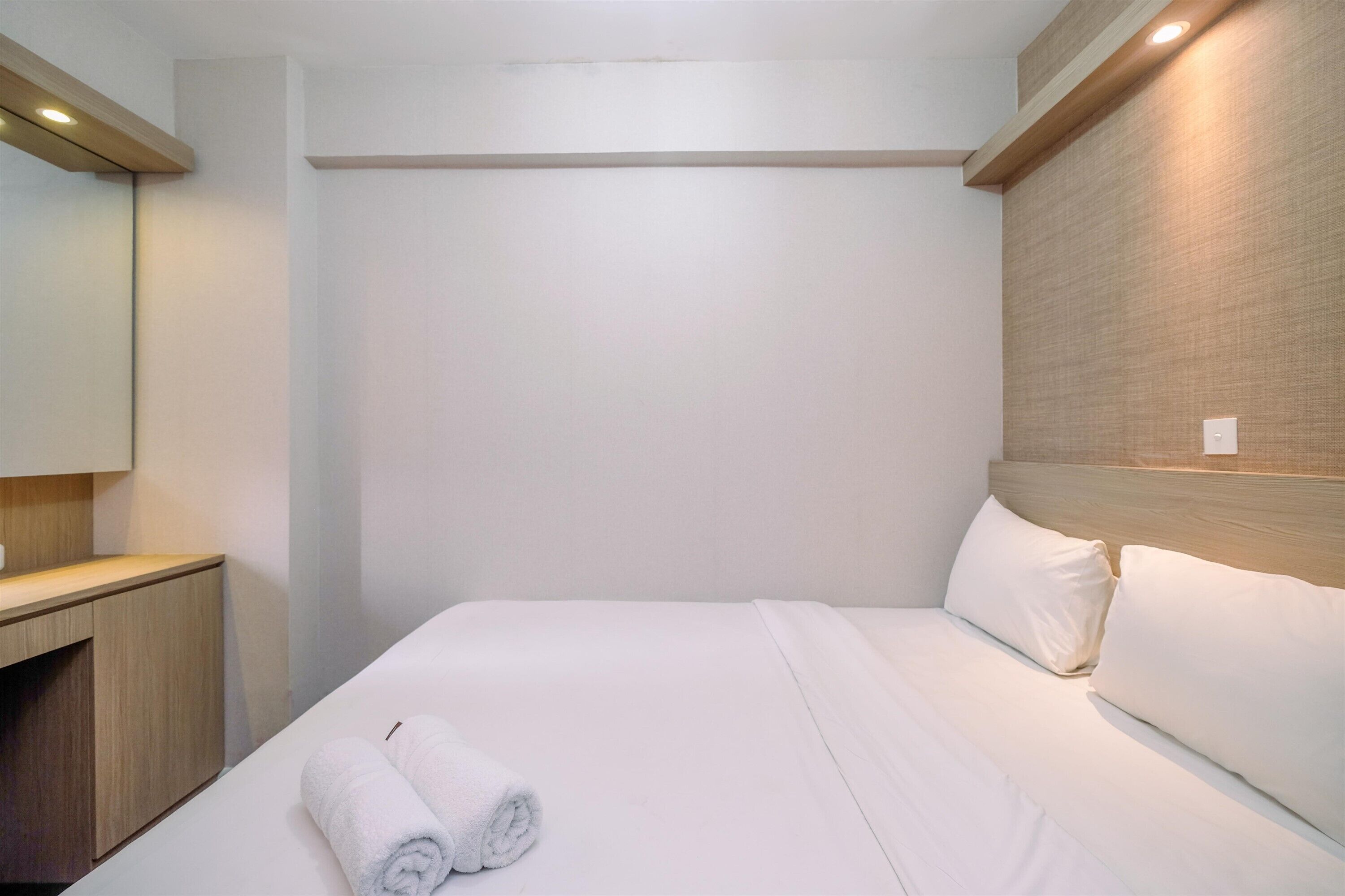 A hotel room with a neatly made bed, a wooden headboard, a wooden nightstand, and a large mirror.