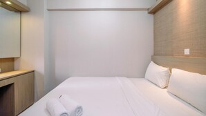 A hotel room with a neatly made bed, a wooden headboard, a wooden nightstand, and a large mirror. - Nice And Fresh 2Br At Bassura City Apartment (Jakarta)