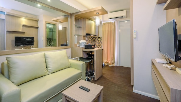 A compact living space with a sofa, a small table, a television, and a kitchenette area. - Nice And Fresh 2Br At Bassura City Apartment (Jakarta)