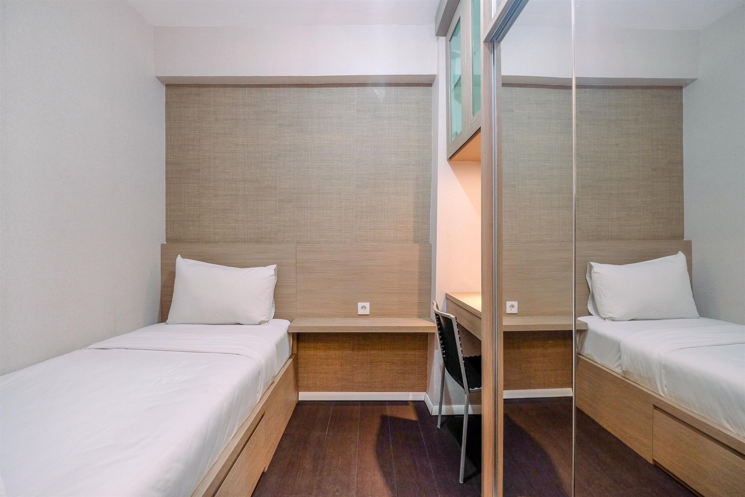 A compact hotel room with two single beds, a small desk, and a mirror.