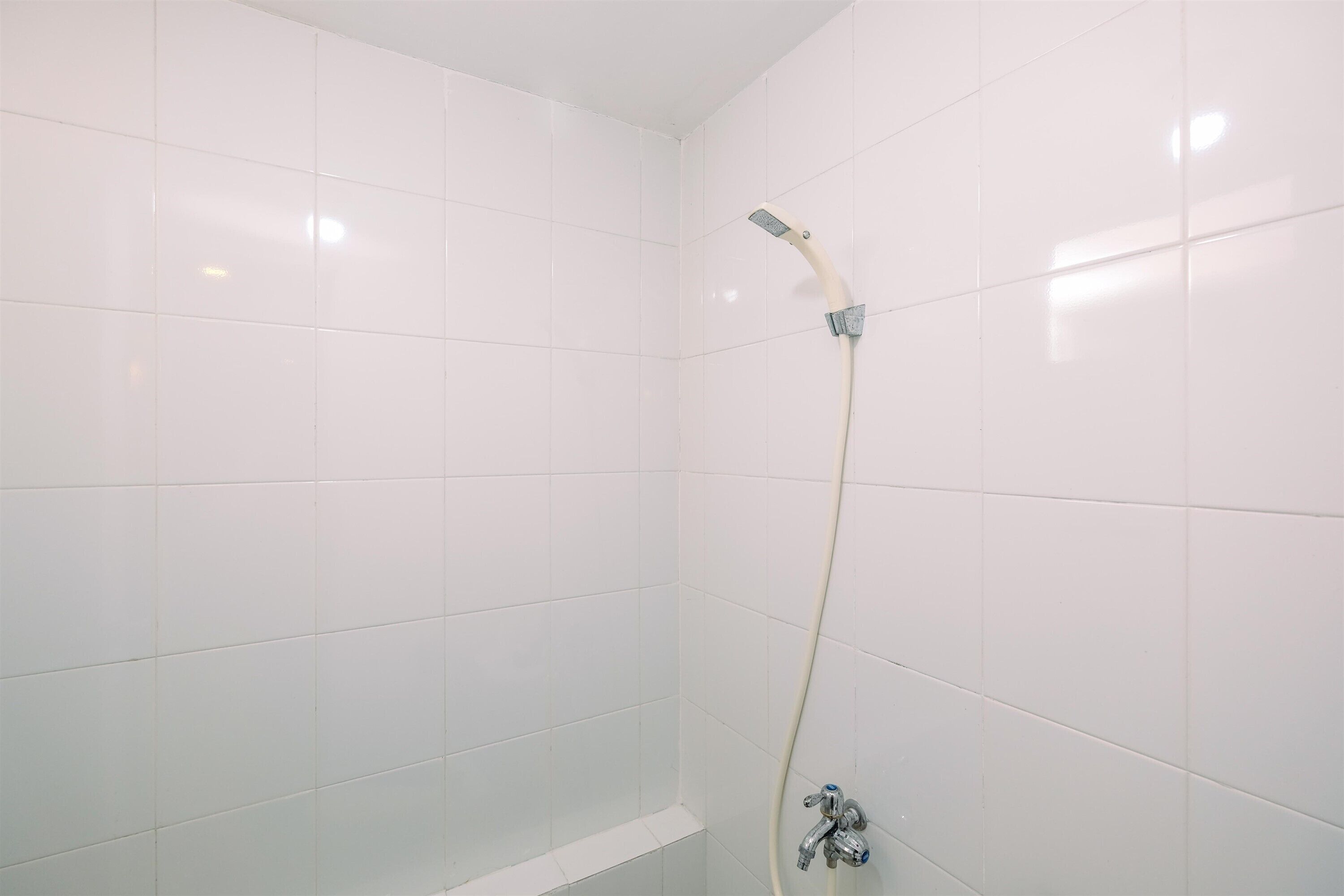 A small, white-tiled shower stall with a handheld showerhead and a wall-mounted faucet.