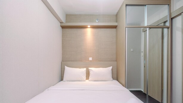 A hotel room with a bed, a headboard with lighting, a mirror, and a sliding door closet. - Nice And Fresh 2Br At Bassura City Apartment (Jakarta)