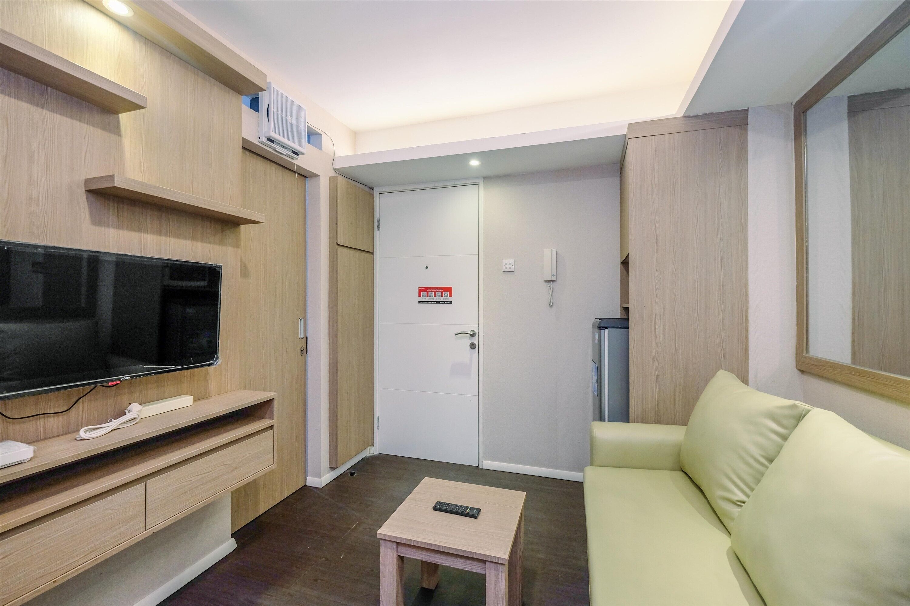 A modern hotel room with a flat-screen TV, a small table with a remote, a sofa, and a wardrobe.