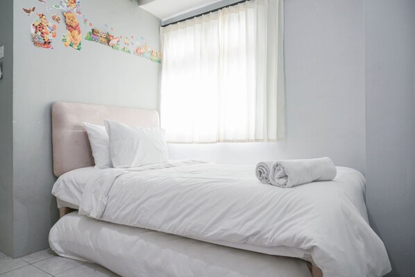 A neatly made bed with white linens and pillows, a window with sheer curtains, and a wall with children's stickers.