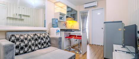 A compact living space with a sofa, a small kitchenette, and a refrigerator.