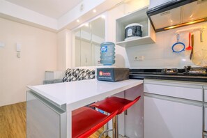 A modern kitchen with white cabinets, a white countertop, and red bar stools. A large water dispenser and a box labeled 'travelio' are visible on the countertop.