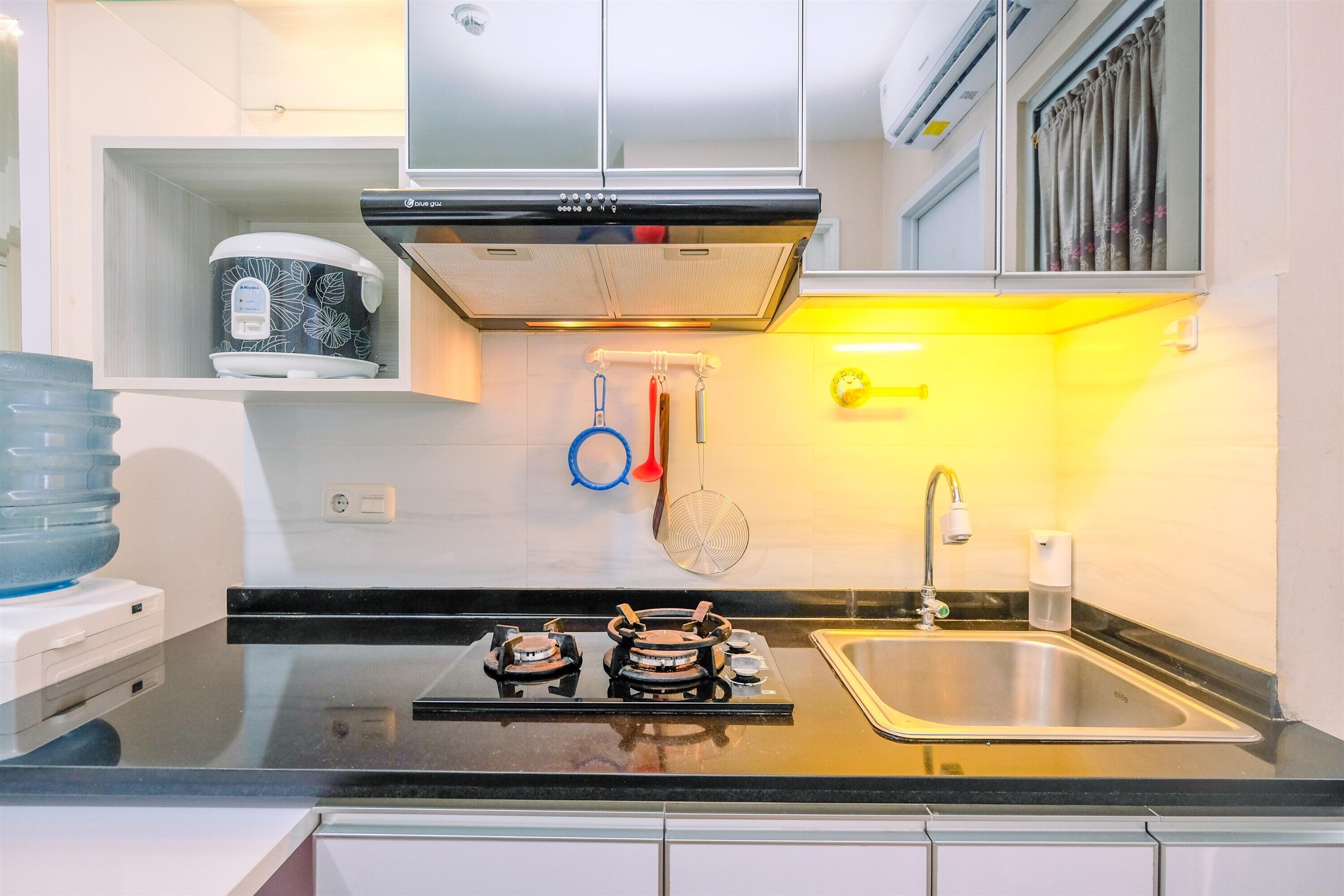 A modern kitchen with a gas stove, stainless steel sink, and a built-in oven. There is a microwave on the countertop, and a kettle hanging on the wall.