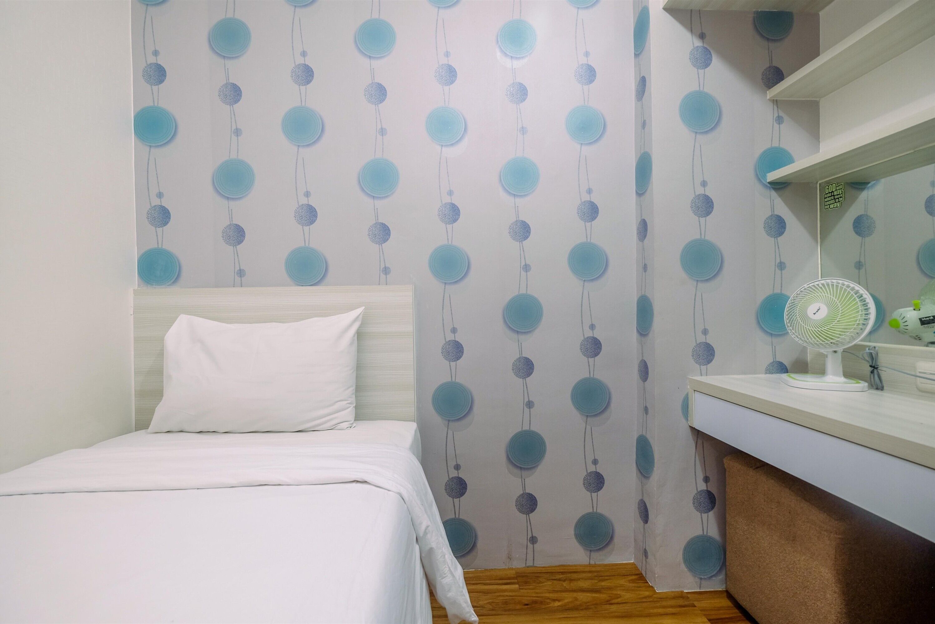 A bedroom with a bed, a bedside table, a mirror, and a wall with a circular pattern.