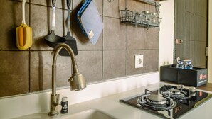 A kitchen with a gas stove, a sink, and various utensils hanging on the wall. - Nice And Warm 1Br At Belmont Residence Puri Apartment (Jakarta)