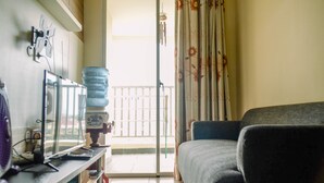 A living room with a sofa, a water dispenser, a fan, and a view of the outside through a sliding door. - Nice And Warm 1Br At Belmont Residence Puri Apartment (Jakarta)