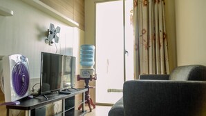 A living room with a TV, a fan, and a water dispenser. - Nice And Warm 1Br At Belmont Residence Puri Apartment (Jakarta)