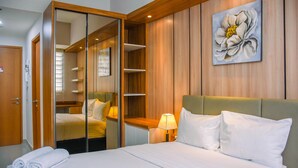 A hotel room with a bed, a nightstand, a lamp, a painting, and a wardrobe with a mirror. - Nice And Cozy Studio At Evenciio Apartment (Depok)
