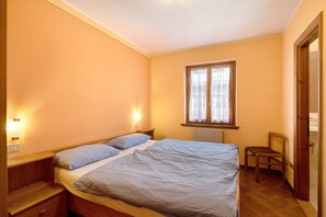 A bedroom with a bed, bedside tables, a chair, a window with curtains, and a radiator.