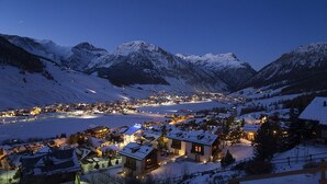 Eine verschneite Bergstadt im Abenddämmerung mit beleuchteten Gebäuden und Blick auf die umliegenden Berggipfel.