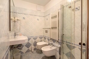 A bathroom with a sink, toilet, bidet, and glass shower enclosure.