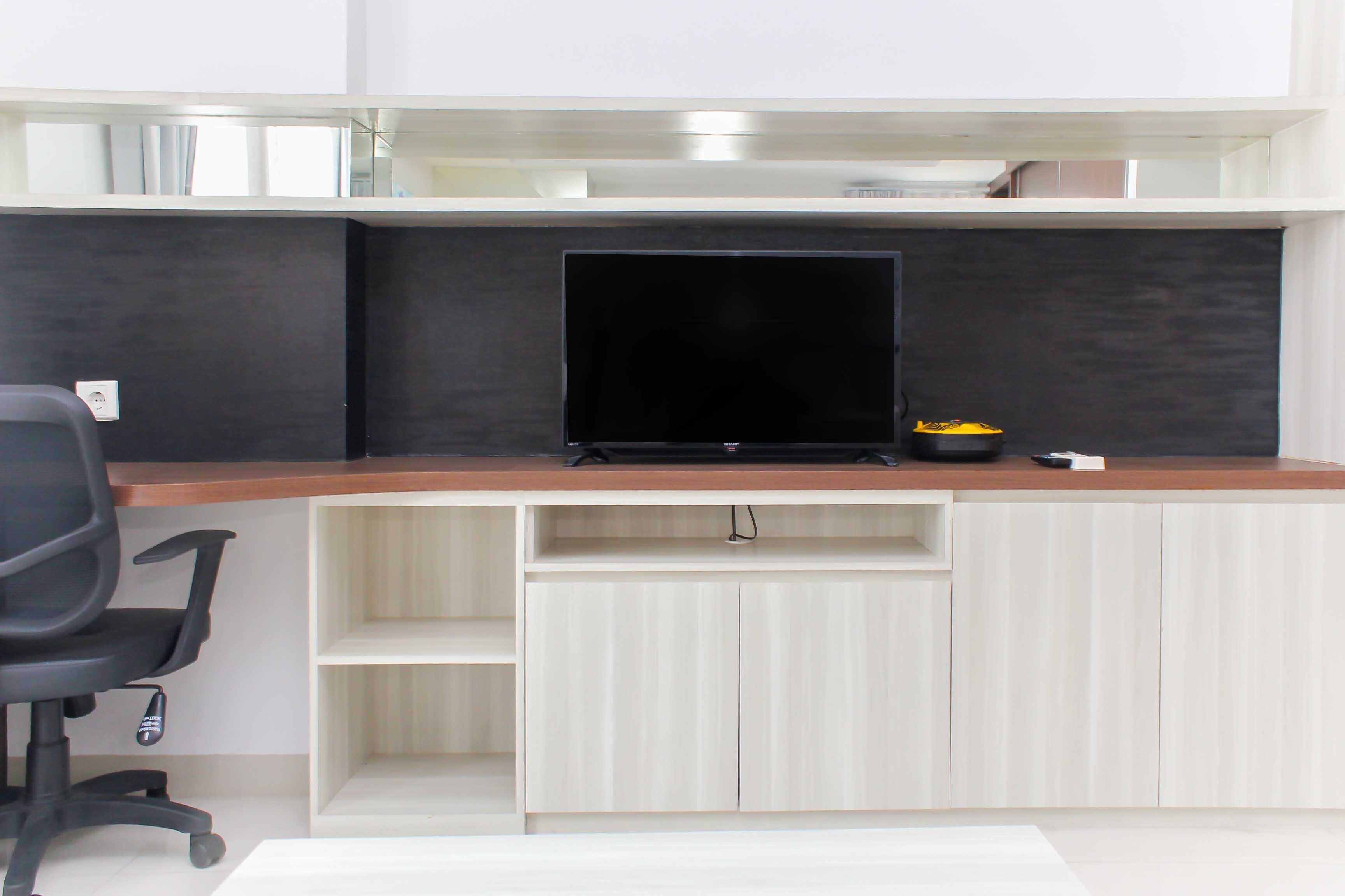 A modern office setup with a flat-screen monitor, a black office chair, and a wooden desk.
