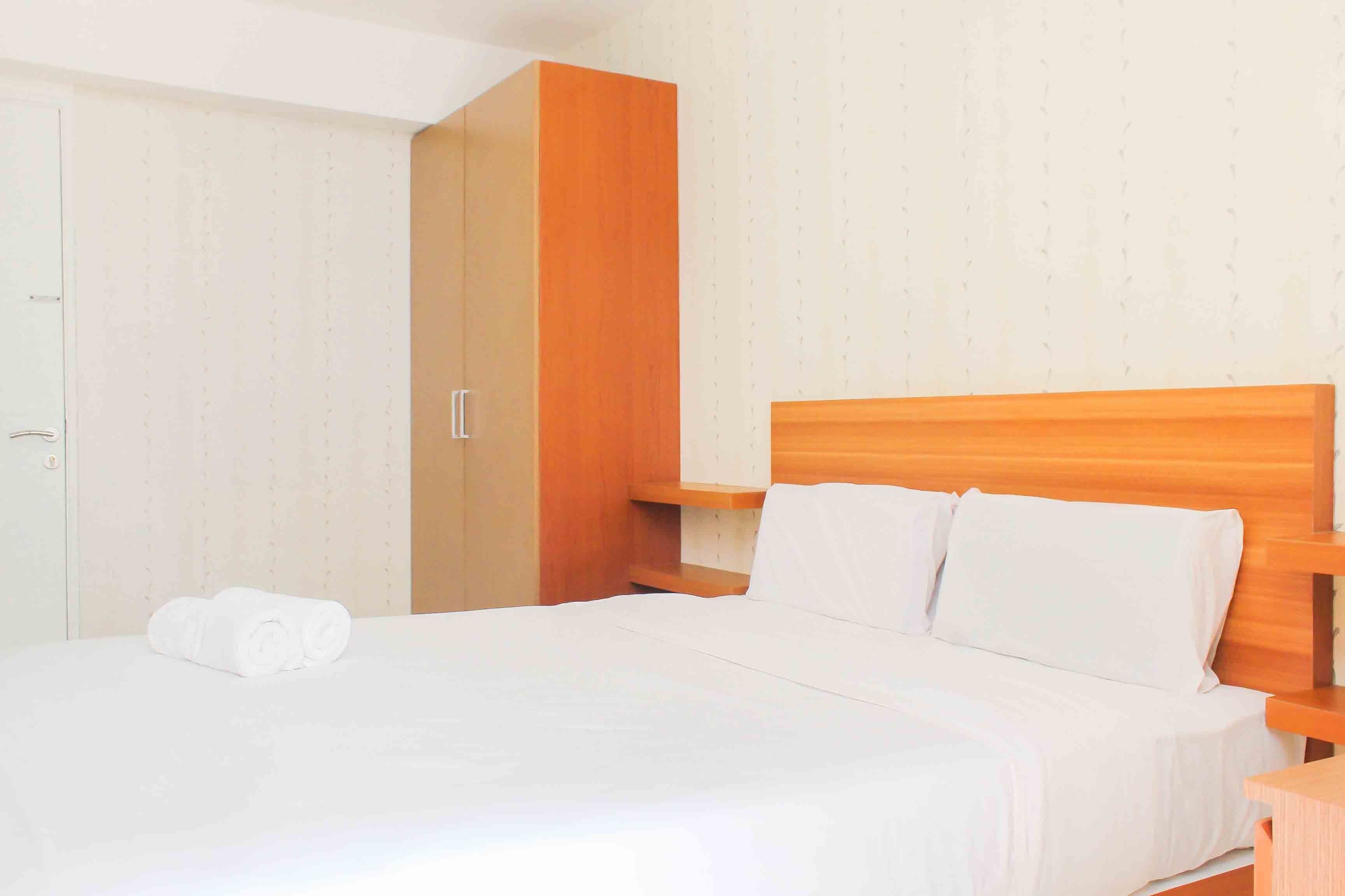 A hotel room with a large bed, wooden headboard, white linens, a wooden wardrobe, and a small bedside table.