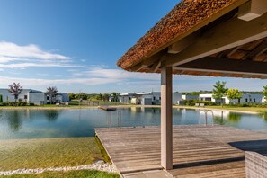 A modern building with a pool, a wooden deck, and a covered area with a thatched roof.
