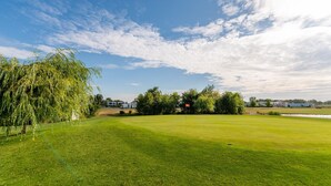 A well-maintained golf course with a clear sky, a large willow tree, and a flag on the green. - Heritage Apartment with Swimming Pond (Zsira)