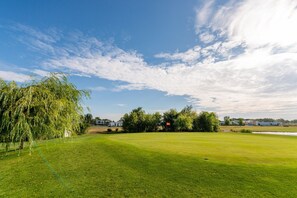 A well-maintained golf course with a clear sky, a large willow tree, and a flag on the green.