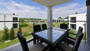 A balcony with a glass table and wicker chairs, overlooking a modern residential area with houses and a swimming pool. - Heritage Apartment with Swimming Pond (Zsira)