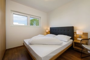 Une chambre à coucher avec un lit, deux lampes de chevet, une chaise et une fenêtre donnant sur des arbres.