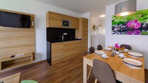 A compact kitchen with a microwave, a flat-screen TV, and a dining area with a table set for two. - Heritage Apartment with Swimming Pond (Zsira)