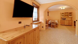 Une cuisine avec un comptoir en bois, un téléviseur fixé au-dessus, une table à manger avec des chaises, et une arche menant à une autre pièce.
