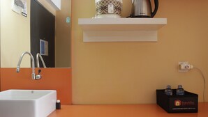 A bathroom with a white sink, a mirror, a towel dispenser, a shelf with a kettle, and a box of toiletries. - Cozy Studio Apartment At The Jarrdin Near Cihampelas Walk (Bandung)