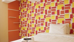 A hotel room with a patterned wall, a bed with white bedding, and a rolled towel on the bed. - Cozy Studio Apartment At The Jarrdin Near Cihampelas Walk (Bandung)