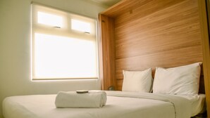 Una cama bien tendida con sábanas y almohadas blancas, un cabecero de madera y una ventana con persianas.