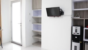 A modern room with a flat-screen TV mounted on the wall, a water dispenser, and built-in shelving. - Spacious And Modern Studio Room Apartment At Grand Asia Afrika (Bandung)