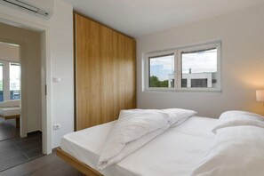 A bedroom with a bed, a wooden wardrobe, a window, and a view of buildings outside. - Apartment in Zsira near Thermal Spa (Zsira)
