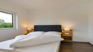 A neatly made bed with white linens and a dark headboard in a room with wooden flooring and white walls. There are two bedside tables with lamps. - Apartment in Zsira near Thermal Spa (Zsira)