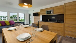 A modern kitchen with wooden cabinets, a built-in microwave, and a dining area with a wooden table set for four. - Apartment in Zsira near Thermal Spa (Zsira)