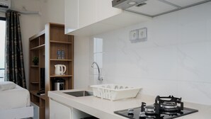 A compact kitchen with a sink, stove, and storage shelves. - Elegant And Comfortable Studio Sky House Bsd Apartment (Pagedangan)