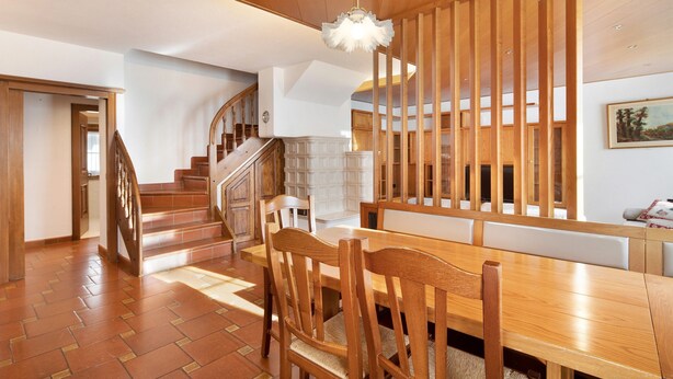 Ein Holzespeisesaal mit Stühlen, einer Treppe und einer dekorativen Deckenleuchte.