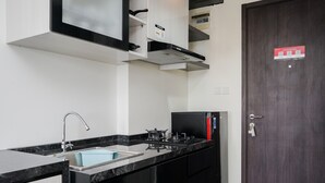 A modern kitchen with black cabinets, a stainless steel sink, and a built-in stove. - Elegant Studio At Bintaro Icon Apartment Near Bintaro Xchange Mall (South Tangerang)