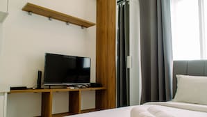 Habitación de hotel con cama, televisor de pantalla plana sobre un soporte de madera, ventana grande con cortinas y estante de madera sobre el televisor.