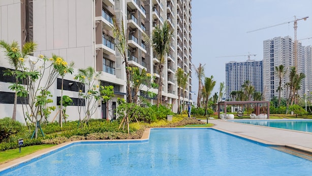 Un moderno edificio residencial con piscina, abundante vegetación y cielo despejado.