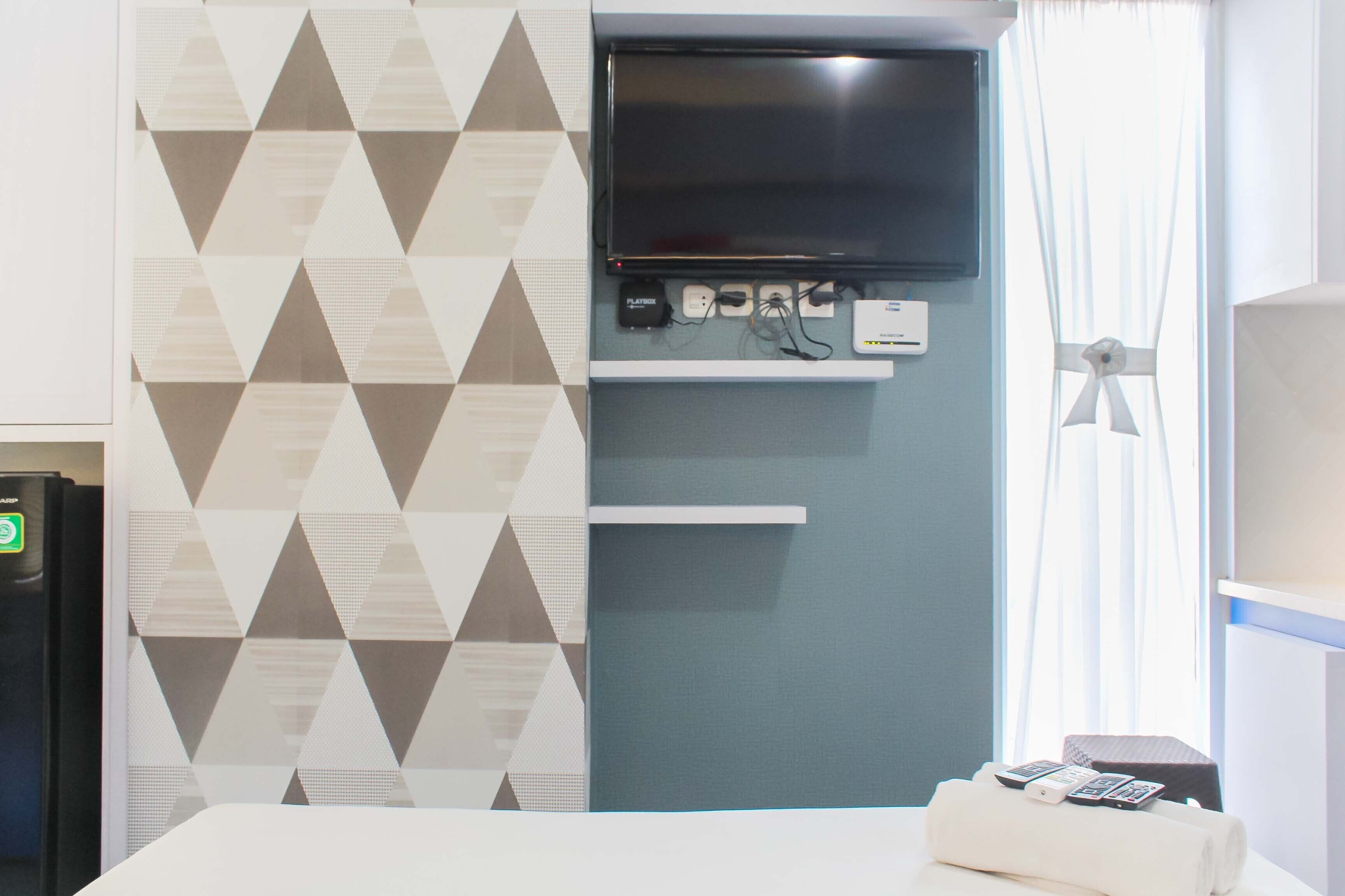 A hotel room with a TV mounted on the wall, a flat-screen TV, a power strip, and a bed with a remote control on it.